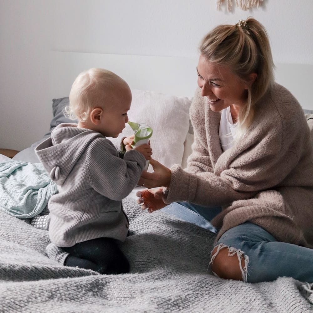 Mama pomaga synkowi oczyścić nosek za pomocą elektrycznego, przenośnego aspiratora do nosa Nosiboo Go